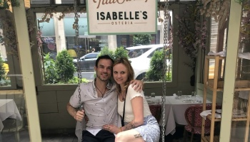 A smiling couple sits together on an indoor swing inside Isabelle's Osteria restaurant.