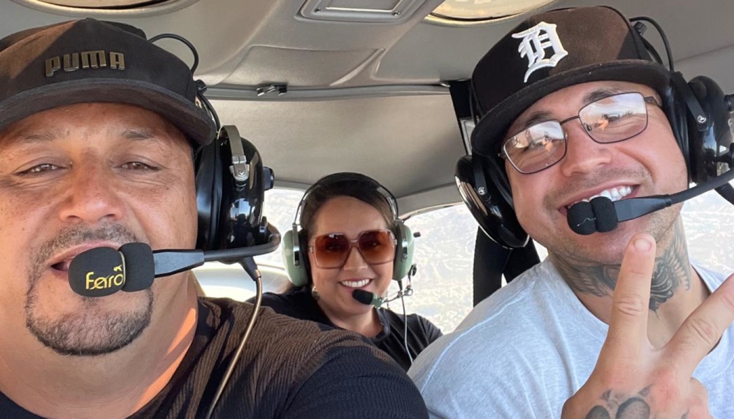Three smiling people wearing aviation headsets and baseball caps pose for a selfie inside a small airplane.