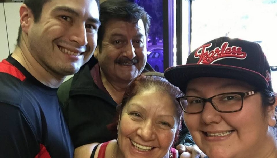 Four smiling family members pose closely together for a happy group selfie.