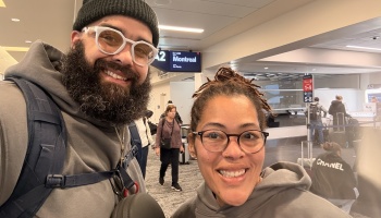 A smiling bearded man and a woman in glasses take a selfie inside an airport terminal near a Montreal gate sign.