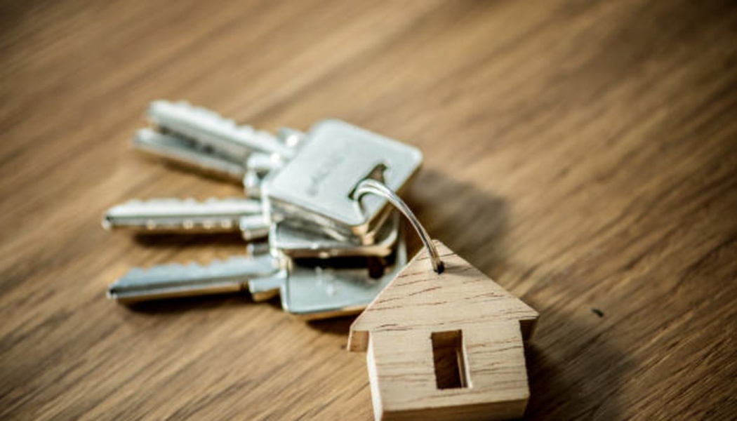 A set of house keys attached to a wooden house-shaped keychain on a wooden surface.