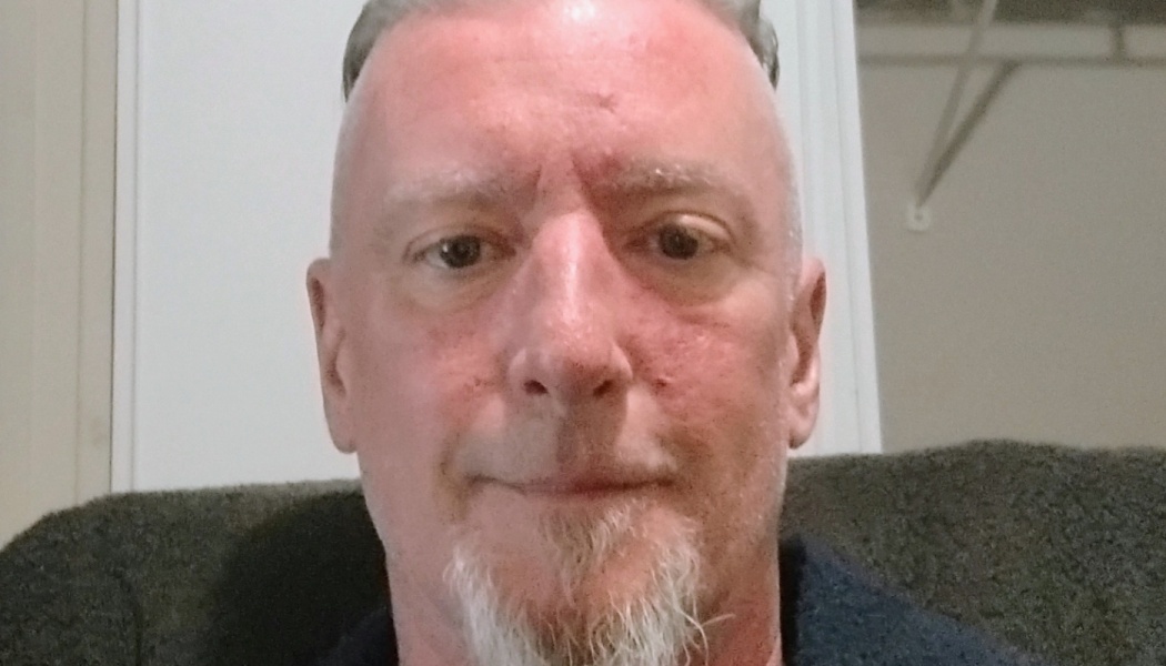 Close-up portrait of a middle-aged man with short grey hair and a white goatee looking directly forward.