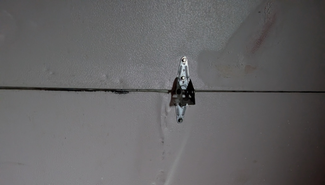 Metal hinge attached to a damaged, dented gray garage door panel.