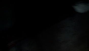 Pitch-black scene with subtle dark textures and a faint white blur in the upper right corner.