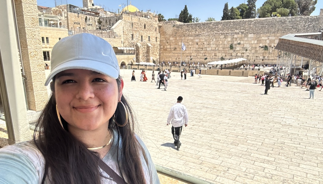 A smiling woman wearing a baseball cap takes a selfie at the Western Wall plaza in Jerusalem.