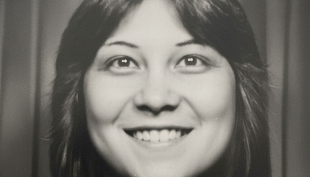 Black and white vintage portrait of a smiling young woman with dark, feathered hair.