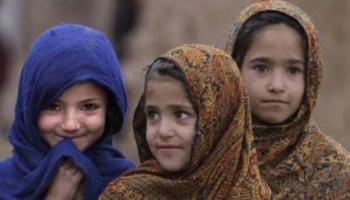 Three young girls wearing headscarves, one in bright blue smiling and two in patterned scarves.