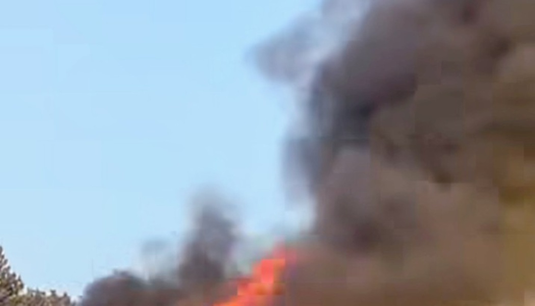 Thick dark smoke and bright orange flames billowing into a clear blue sky.
