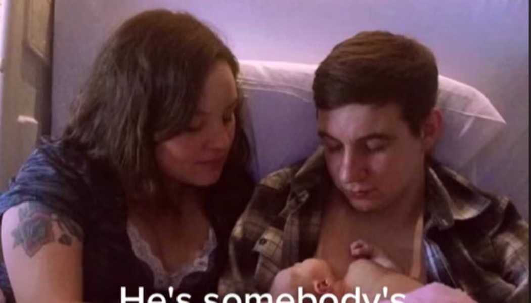 A couple sitting together in bed, gazing lovingly down at their newborn baby held skin-to-skin.