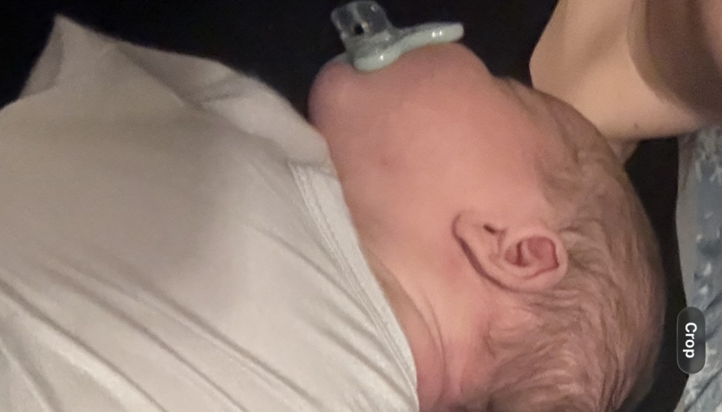 Close-up side profile of a newborn infant resting with a pacifier in its mouth.