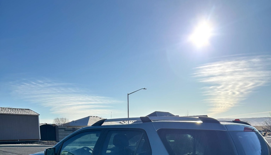 Silver SUV parked in a residential neighborhood under a bright, sunny blue sky with thin wispy clouds.