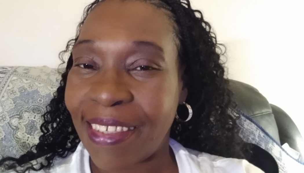 Close-up portrait of a smiling Black woman with long braided hair and hoop earrings.