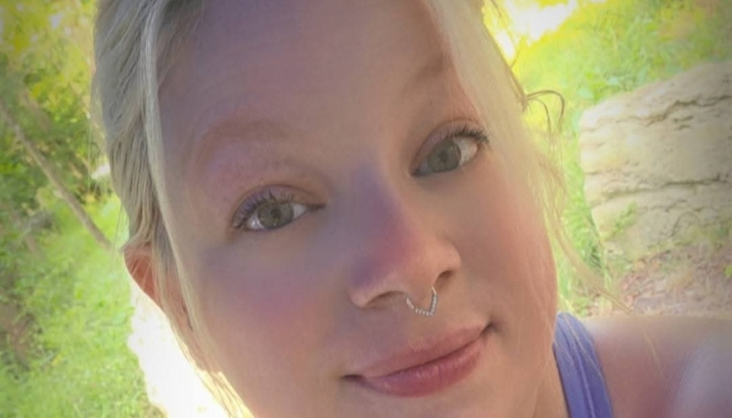 Close-up portrait of a blonde woman with a septum nose piercing smiling outdoors.