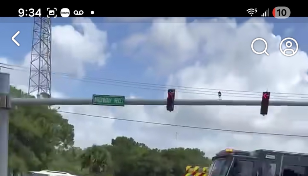 Green street sign for Midway Rd and traffic lights mounted at a road intersection under a cloudy sky.