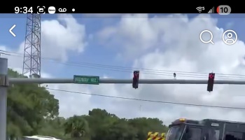 Green street sign for Midway Rd and traffic lights mounted at a road intersection under a cloudy sky.