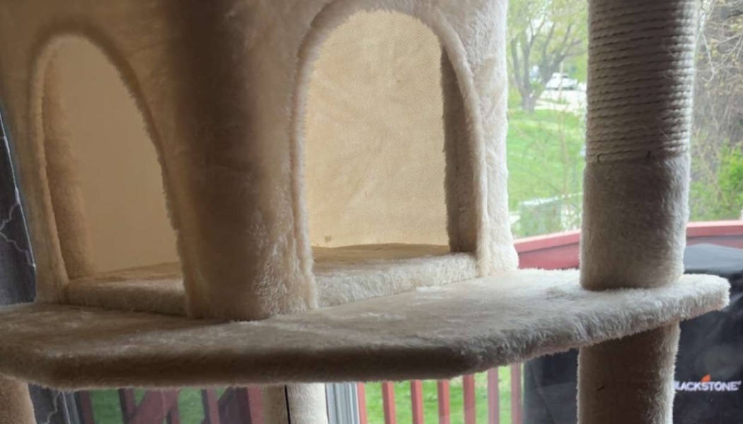 Off-white plush cat condo with arched doorways and a scratching post next to a window.