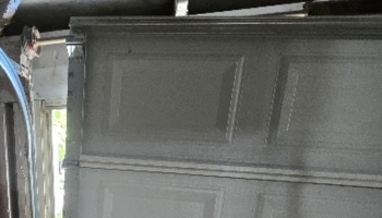 A damaged grey garage door hanging off its track inside a home garage.