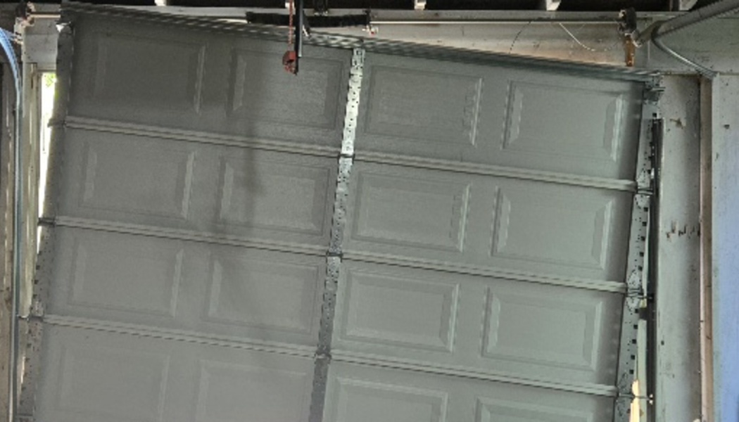 A broken white garage door off its tracks and hanging crookedly inside the frame.
