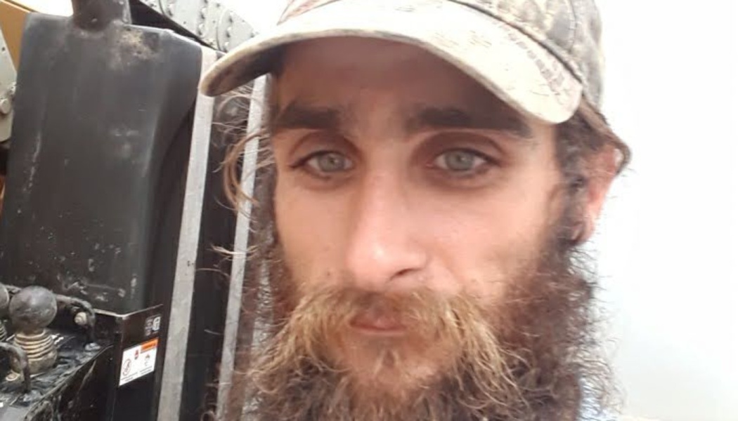 Close-up of a man with light eyes and a full beard, wearing a camouflage baseball cap.