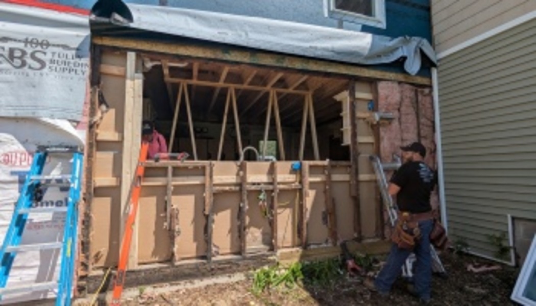 Two construction workers rebuilding the exposed wall frame of a home under renovation.
