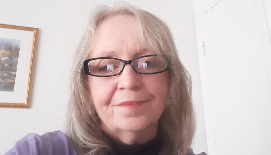 Woman with shoulder-length blonde hair and black glasses looking at the camera with a gentle smile.
