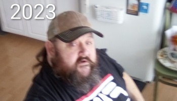 Bearded man wearing a baseball cap indoors, with the year 2023 displayed in the top left corner.
