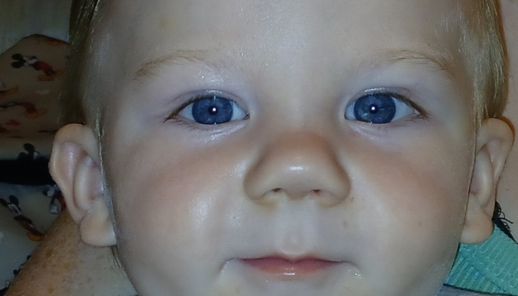 Close-up portrait of a toddler with fair skin, light hair, and vivid blue eyes looking directly at the camera.