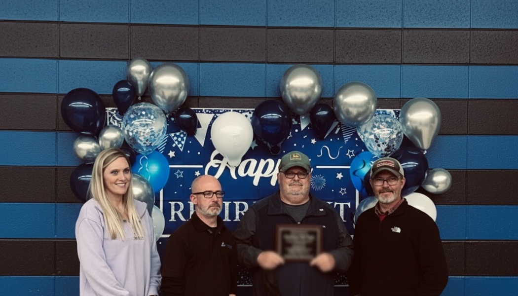 Four people pose in front of a Happy Retirement balloon display as a man holds an award plaque.