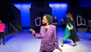 Young actor in a bright purple suit holding a prop on a theatrical stage lit in blue.