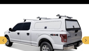 White 4x4 pickup truck fitted with a white commercial camper shell and roof rack crossbars.