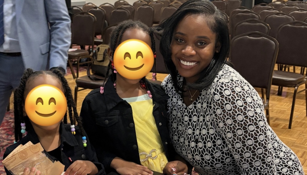 A smiling woman poses with two young girls with emoji-covered faces inside an event venue.