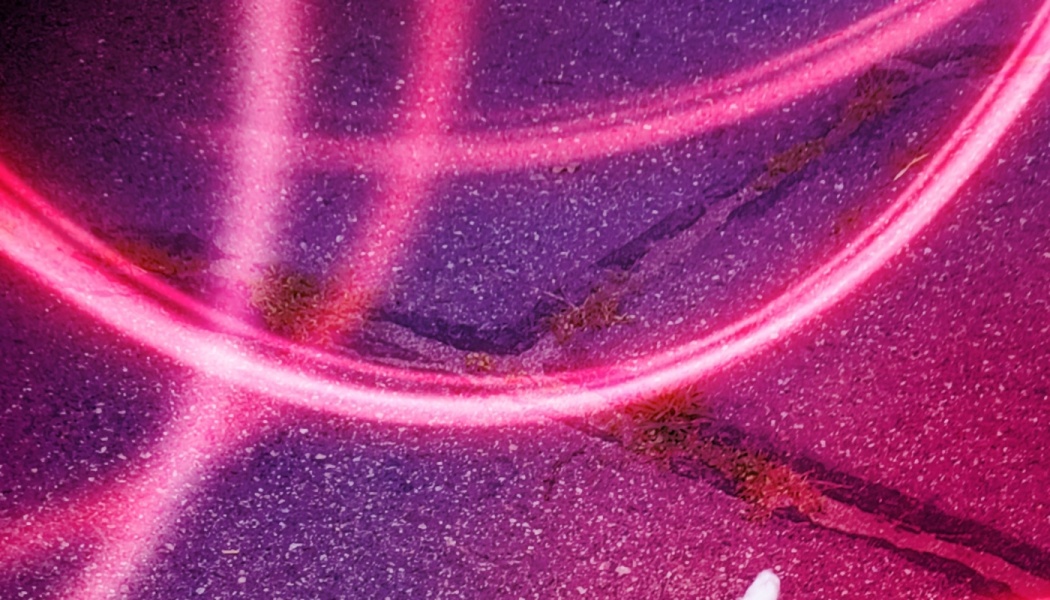 Vibrant pink neon light trails sweeping across textured dark asphalt.