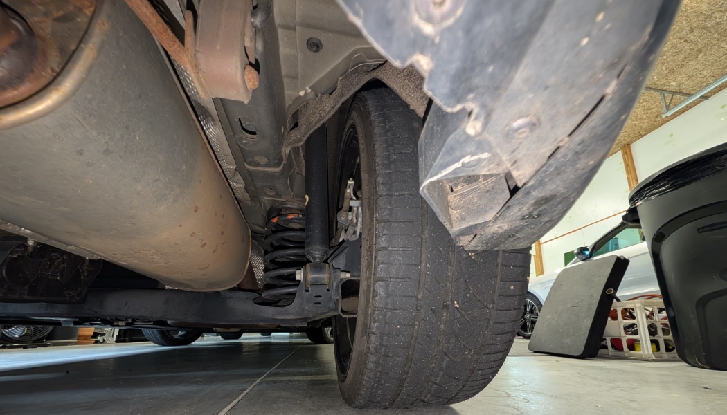 Low-angle view of a vehicle's undercarriage showing the tire, suspension coil spring, and exhaust muffler.