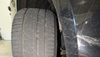 Close-up of a worn car tire tread positioned under a dark vehicle's fender.