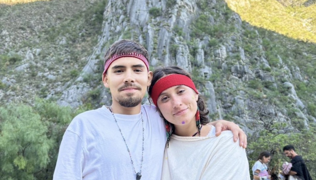 A smiling young man and woman wearing red headbands pose together in front of a rocky mountain cliff.