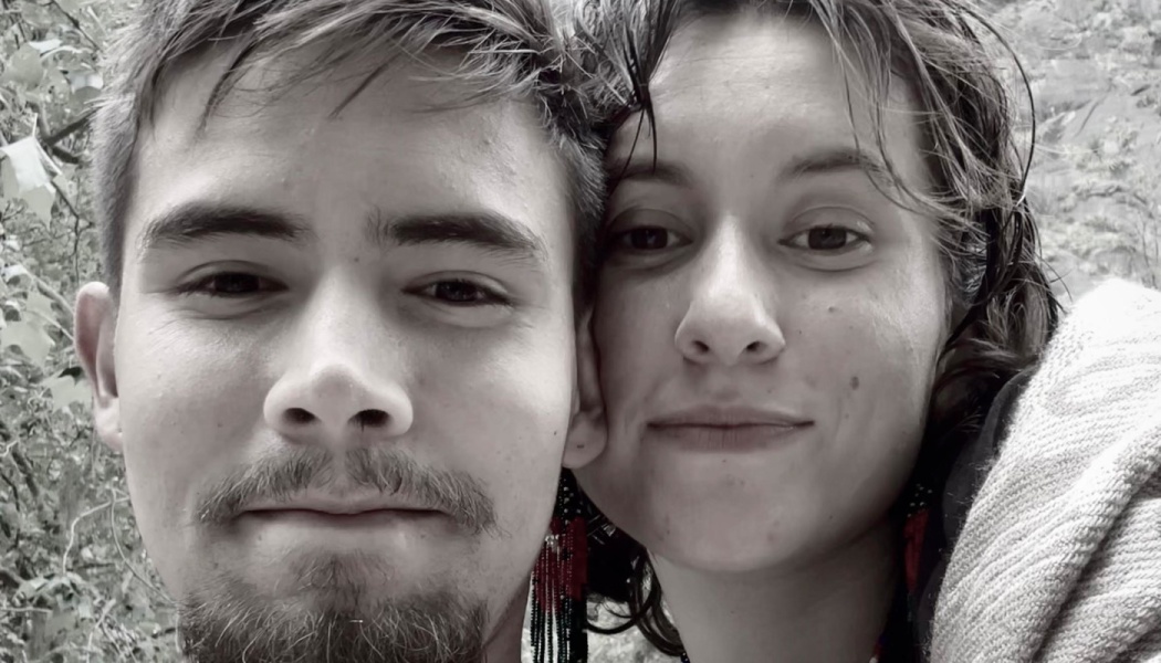 Black-and-white close-up portrait of a young couple leaning cheek to cheek outdoors.