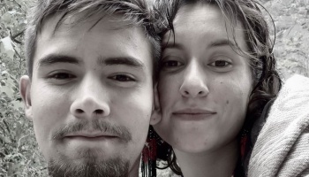 Black-and-white close-up portrait of a young couple leaning cheek to cheek outdoors.