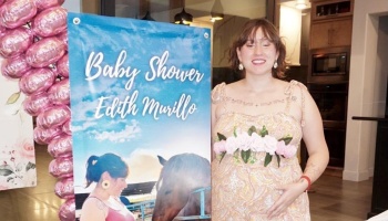 Smiling pregnant woman standing next to a blue "Baby Shower Edith Murillo" banner with pink balloons.