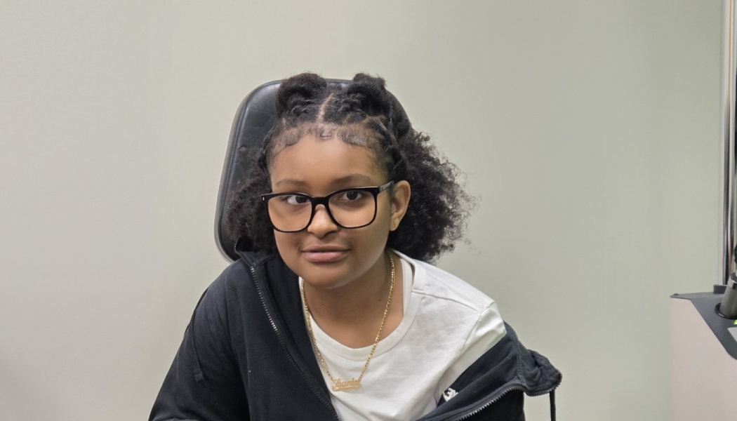 Young girl with black-framed glasses and a space-bun hairstyle sitting in an examination chair.