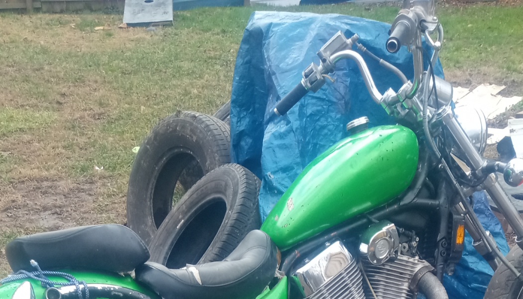 Bright green motorcycle parked outdoors next to spare tires and a blue tarp.
