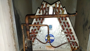 Old, corroded HVAC A-coil evaporator with rusty copper piping inside a metal duct.