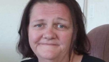 Close-up of a middle-aged woman with dark hair and blue eyes looking at the camera.