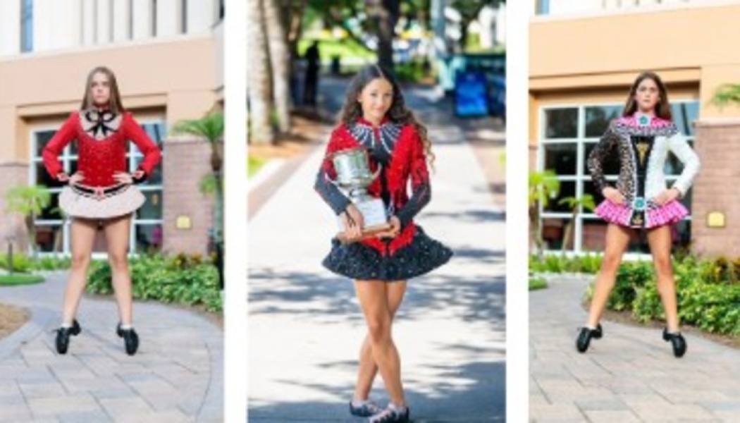 Three Irish dancers in vibrant solo dresses posing outdoors, one holding a large championship trophy.