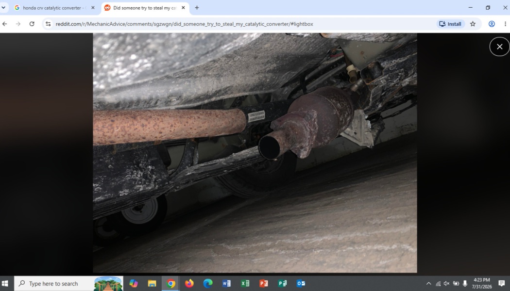 Underside of a vehicle showing a severed, rusty exhaust pipe cut near the catalytic converter.