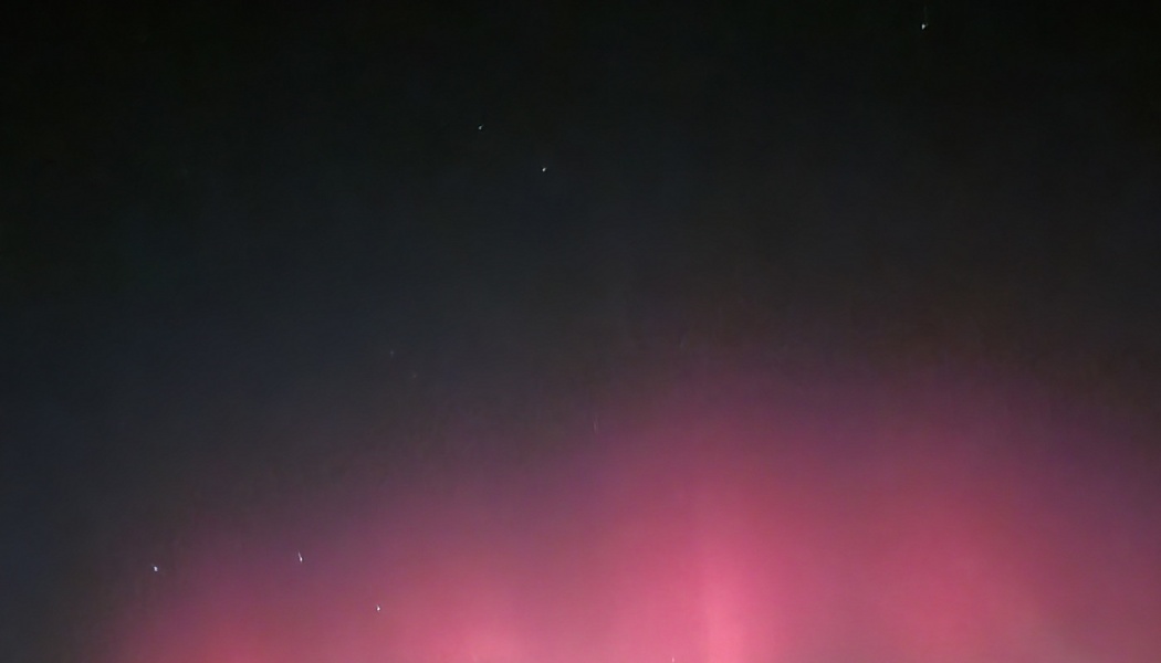 Vibrant pink northern lights glowing under a dark night sky filled with distant stars.