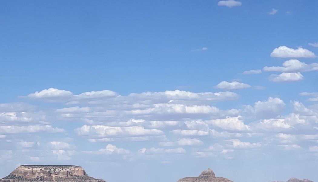 Flat-topped rock mesas beneath a vast blue sky filled with scattered white clouds.