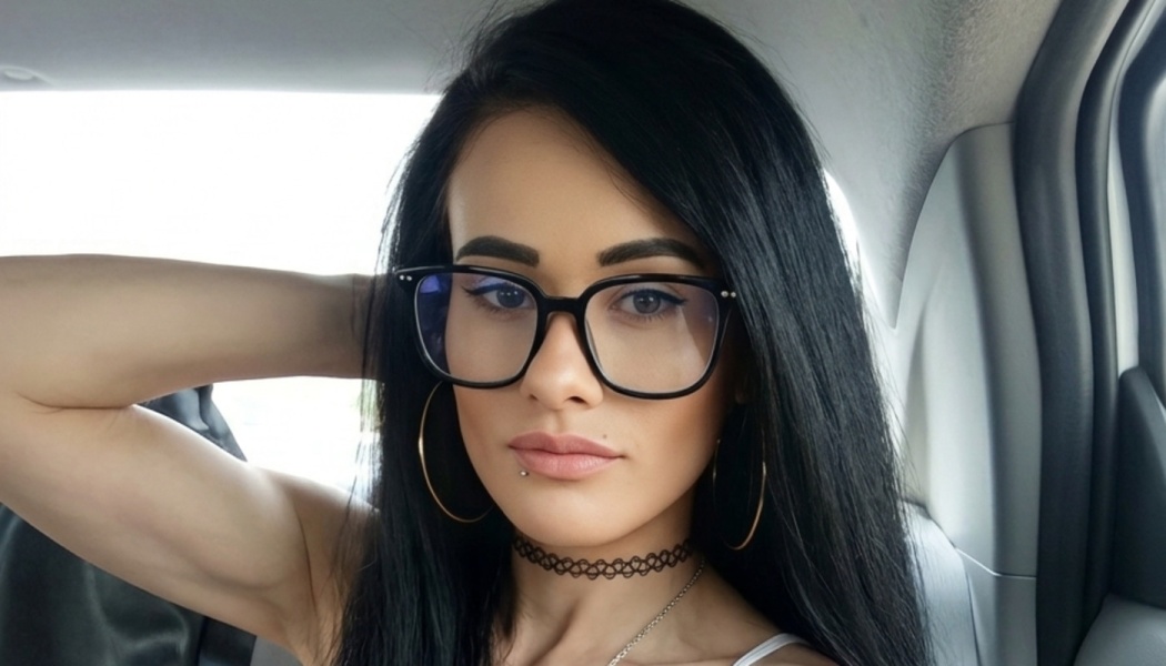 Young woman with long black hair, black-framed glasses, hoop earrings, and a black choker posing inside a car.