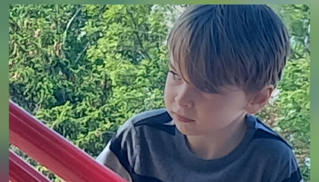 A young boy looking thoughtfully off to the side with vibrant green foliage in the background.
