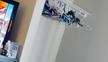 Assorted plastic clothes hangers hanging on a white closet rack next to a TV.