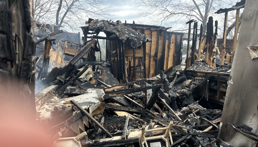 Charred remnants and collapsed wooden beams of a home completely destroyed by fire.